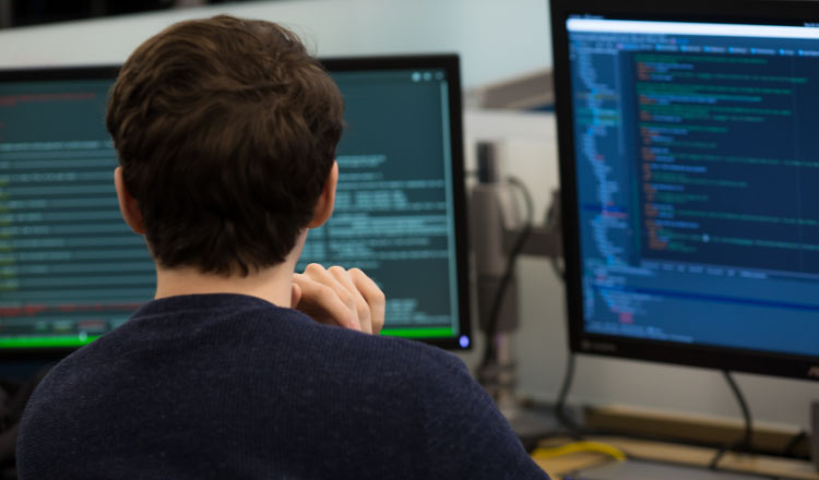 A technical professional works at a desk with computor monitors showing code